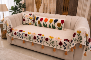 Designer embroidered sofa cover with colorful floral patterns and tassel edges draped over a modern beige curved sofa in a luxury living room.